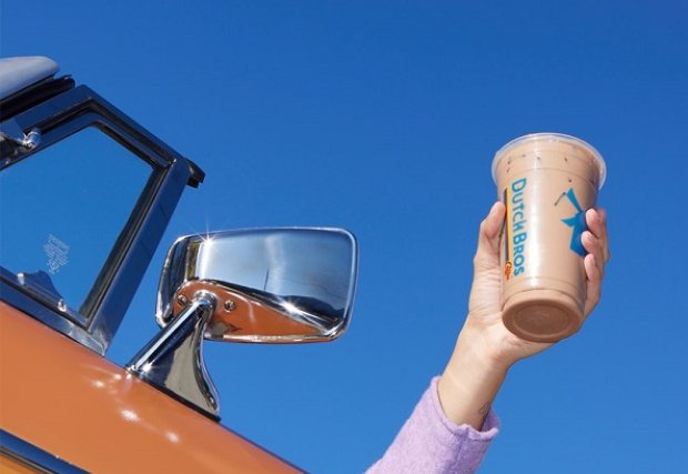 A hand holding a Dutch Bros cup out a car window on a sunny day 